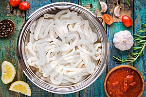 Fresh raw squid rings in a steel bowl on a wooden table