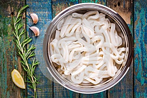 Fresh raw squid rings in a steel bowl on a wooden table