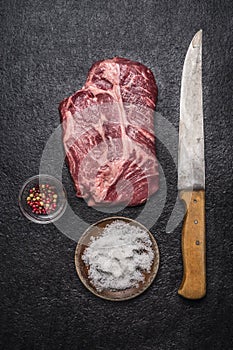 Fresh raw steak with red pepper and salt with carving knife on a dark rustic background top view