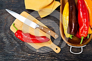 Fresh raw sweet pepper bell pepper on a cutting board with a knife. Ready to cook. Dark wooden table, top view