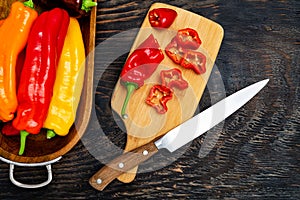 Fresh raw sweet pepper on a cutting board with a knife. Chopped pepper pieces are ready to cook. Dark wooden table,