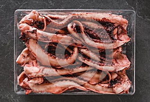 Fresh raw tentacles of octopus on box over dark stone background. Seafood, top view, flat lay, copy space