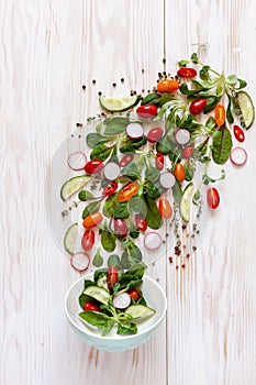 Fresh raw tomatoes, cucumbers, baby spinach and seasonal greens. Top view, close-up on white wooden background