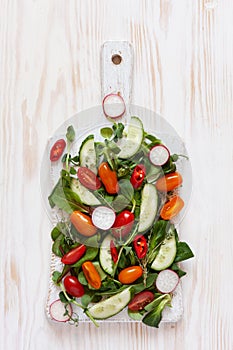 Fresh raw tomatoes, cucumbers, baby spinach and seasonal greens. Top view, close-up on white wooden background