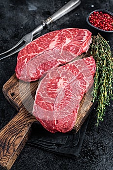 Fresh Raw Top Blade or flat iron beef meat steaks on a butcher cutting board. Black background. Top View