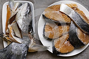 Fresh raw trout or salmon fish slices steak in white plate, head, fillet in glass bowl, with spices on stone background. Creative