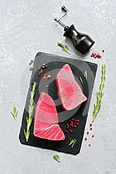 Fresh raw tuna steak with spices on a black slate plate. gray background. Top view, flat lay