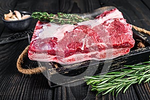 Fresh Raw veal short ribs in a wooden tray with herbs. Black wooden background. Top view