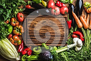 Fresh raw vegetable ingredients for healthy cooking or salad making with rustic wood board in center, top view, copy photo