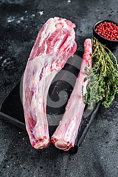 Fresh Raw whole Beef veal Oxtail Meat on marble board with herbs. Black background. Top view