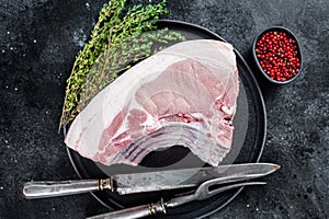 Fresh Raw whole rack of pork loin chops with ribs on a plate with meat fork. Black background. Top view