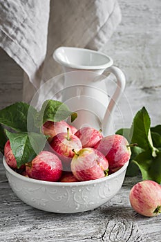 Fresh red apples in a white bowl and enameled pitcher
