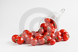 Fresh red baby plum or cherry tomatoes pour out of a transparent mug. The concept of making natural tomato juice. White background