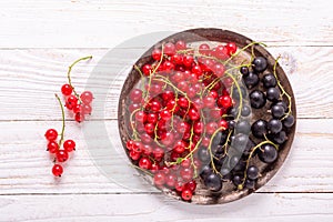 Fresh red and black currant on the vintage metal plate on a white wooden background Top view