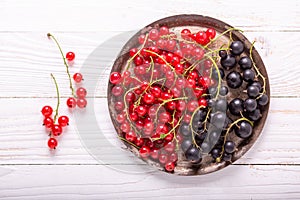 Fresh red and black currant on the vintage metal plate on a white wooden background Top view