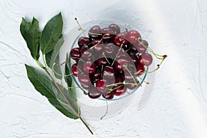 Fresh red cherries in a bowl on a white background with green branch cherry tree. top view