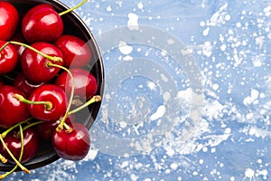 Fresh red cherries in ceramic bowl on blue background.Top view.