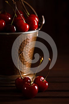 Fresh red cherries in copper bucket on dark wooden background