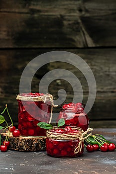 Fresh red cherries fruit on wooden background. Jar of cherry jam and sour cherries. Berries cherry with syrup. Canned fruit. place