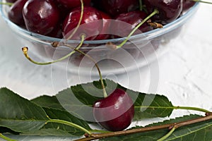 Fresh red cherries with green leaves in a bowl on a white background