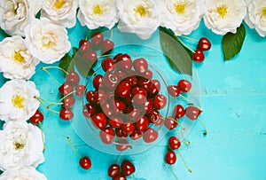 Fresh red cherry in a bowl and white roses on an old painted wooden table as a bright colorful summer background for seasonal