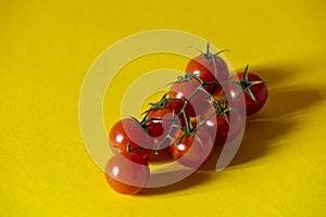 Fresh red cherry tomatoes with green stems isolated on yellow background