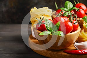 Fresh red cherry tomatoes with raw pasta, basil, chili pepper and garlic for Italian food