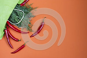 Fresh red chili peppers and dill greens in a paper bag on an orange background. Bag for shopping healthy food. View from above