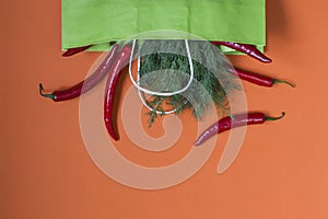 Fresh red chili peppers and dill greens in a paper bag on an orange background. Bag for shopping healthy food. View from above