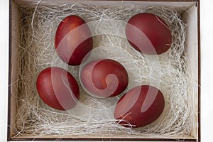 Fresh red eggs and some straw in a wooden crate on a white background.