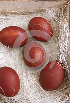 Fresh red eggs and some straw in a wooden crate on a white background.