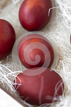 Fresh red eggs and some straw in a wooden crate on a white background.