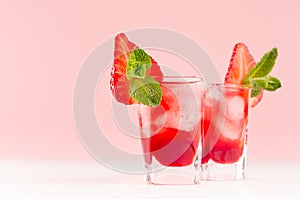 Fresh red fruit cocktail with ice cubes, strawberry slice, green mint in elegant misted shot glasses on soft light pink color.