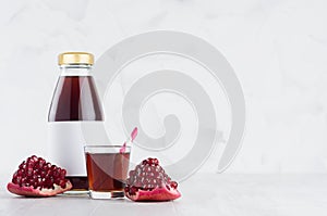 Fresh red garnet juice in glass bottle mock up with blank label, straw, wine glass, fruit piece on white wood table in light.