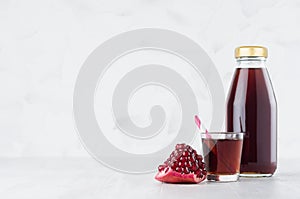 Fresh red garnet juice in glass bottle mock up with straw, wine glass, fruit piece on white wood table in light interior, template