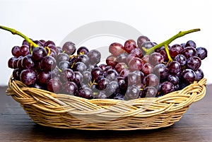 Fresh red grapes without seeds in a wooden basket placed on a table and a white background