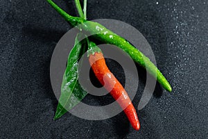 Fresh red and green chili with leaf and drops of water on black table