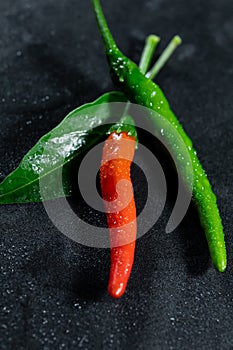 Fresh red and green chili with leaf and drops of water on black table, Portrait photo