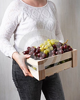 Fresh red and green  grapes fruit in wooden box in the hands of a girl in light clothes on white  background