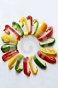 Fresh red, green and yellow bell peppers capsicum has been cut into pieces arranged in a circle isolated on white background. Co