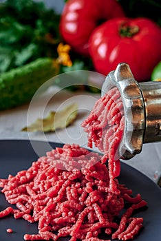 Fresh red meat mincing with old metal manual grinder, viewed in close-up on grey stone background .