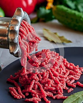 Fresh red meat mincing with old metal manual grinder, viewed in close-up on grey stone background .