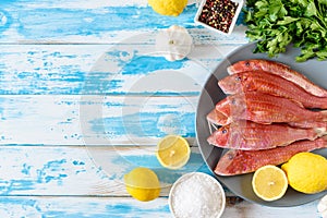 Fresh red mullet fish on blue wooden background with herbs