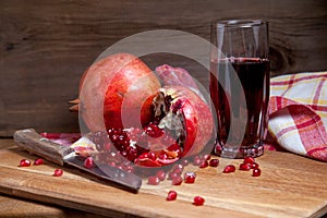 Fresh red pomegranate with vintage knife and glass of fresh rudy juice on a wooden background