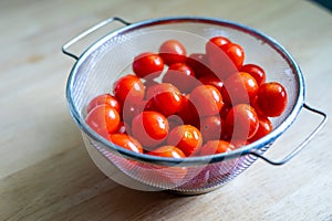 Fresh red ripe cherry tomatoes in a stainless colander on a wooden table, prepare for cooking.
