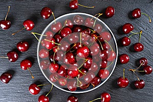 Fresh red ripe sweet cherry on plate on black slate background.