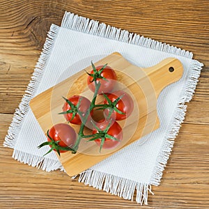Fresh red ripe tomatoes cherry with water drops on branch on wooden background with rustic chopping board in center