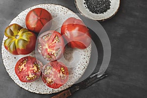 Fresh red ripe tomatoes on a wooden cutting board with black Thursday salt, dark rustic background. Tomatoes being cut