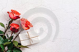 Fresh red roses and a box in craft paper on a textured gray background. Holiday gift, congratulations. Top view