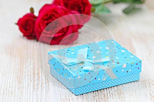 Fresh red roses and gift box on wooden table